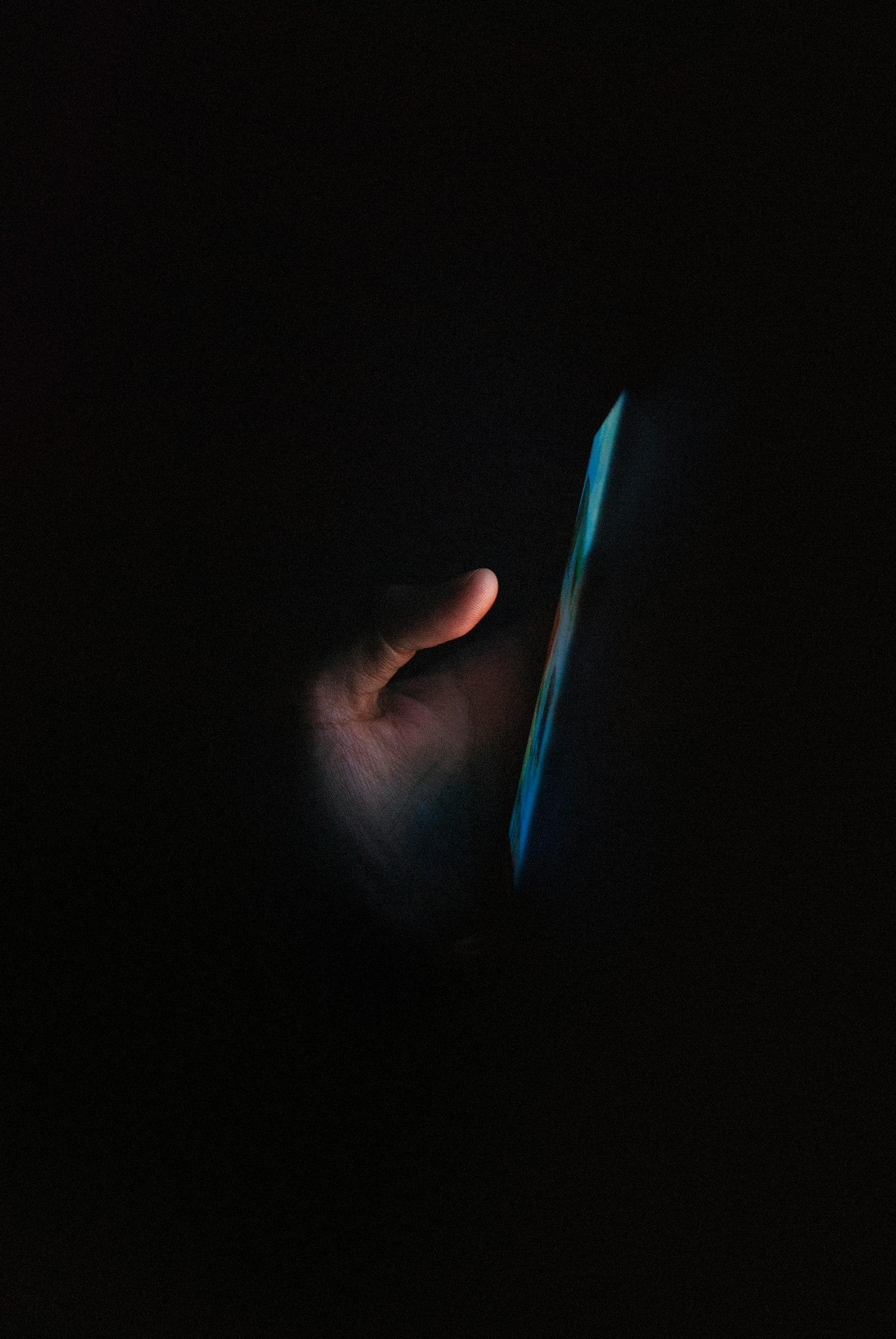 A hand holding a phone in a dark room with the screen glowing blue