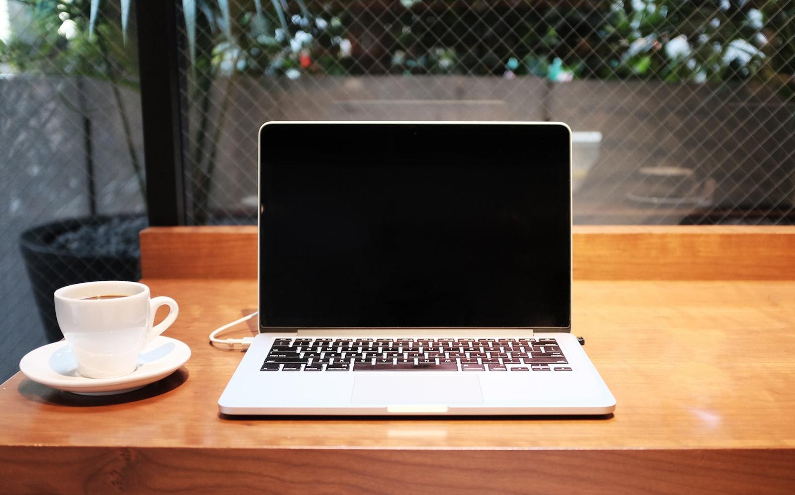 A laptop and coffee on a wooden cafe table, late afternoon light