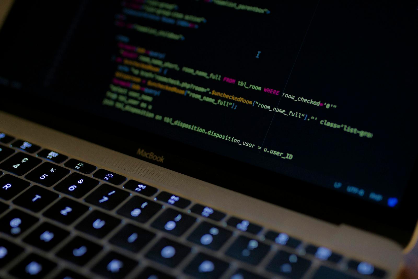 A developer's MacBook displaying syntax-highlighted code in a dark room