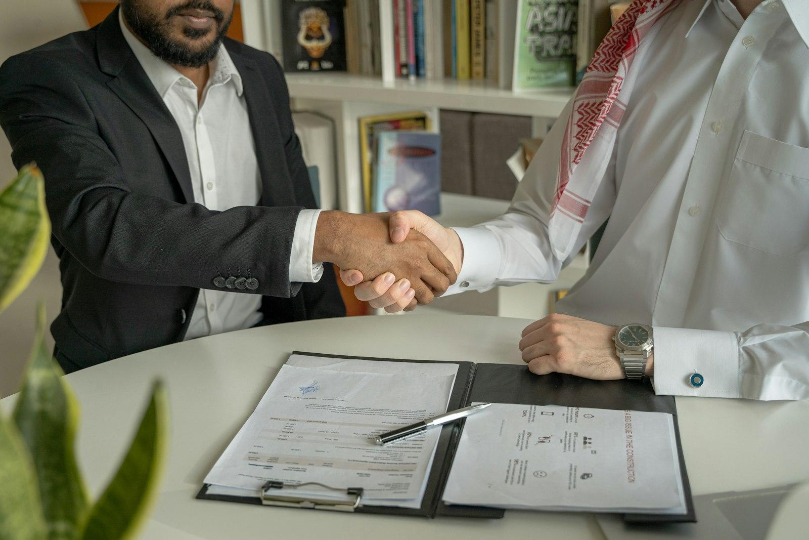 Two professionals shaking hands over signed documents in a bright office
