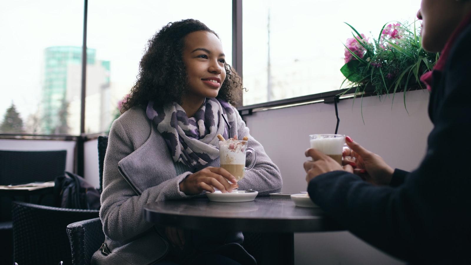 Two people having a warm conversation over coffee at a window-side cafe table